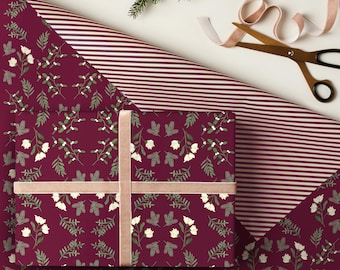 May include: A wrapped gift box with a burgundy floral pattern and a light pink ribbon. The wrapping paper has a floral design with white flowers and green leaves. A roll of striped wrapping paper and scissors are also visible.