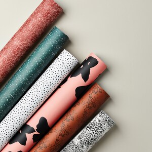 May include: Six rolls of wrapping paper with different patterns. The patterns include black and white polka dots, black and white floral designs, and black and pink floral designs.