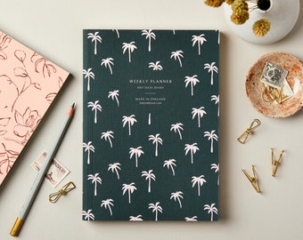 May include: A dark green weekly planner with a palm tree pattern. The planner has the text "Weekly Planner" and "Any Date Diary" on the front cover. It also says "Made in England".