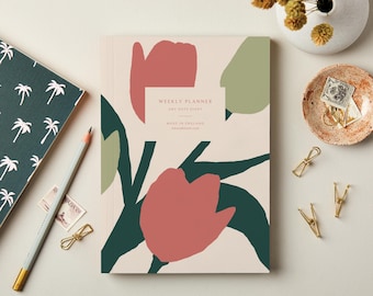 May include: A weekly planner with a floral design in shades of red, green, and beige. The planner has the text "WEEKLY PLANNER ANY DATE DIARY MADE IN ENGLAND". A pencil, stamps, and paper clips are also visible.