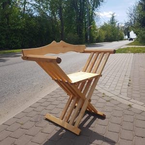 May include: A wooden folding chair with a simple design. The chair is made of light-colored wood and has a slatted seat and back.
