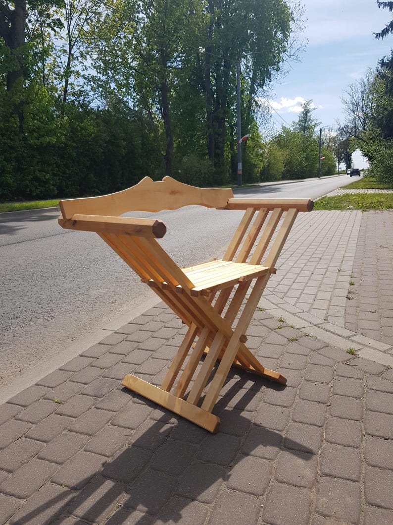 May include: A wooden folding chair with a simple design. The chair is made of light-colored wood and has a slatted seat and back.