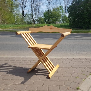 May include: A wooden folding chair with a curved back and a simple design. The chair is made of natural wood and has a light brown color.