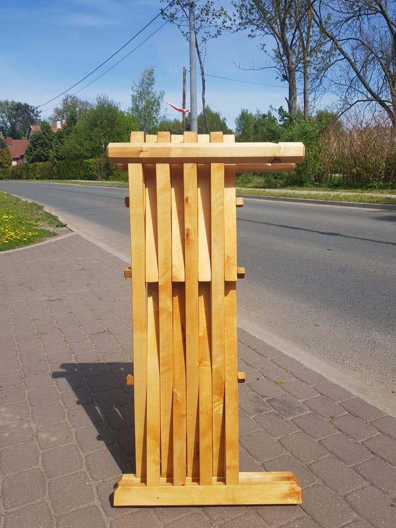May include: A wooden folding chair with a natural finish. The chair is folded up and standing on a sidewalk.
