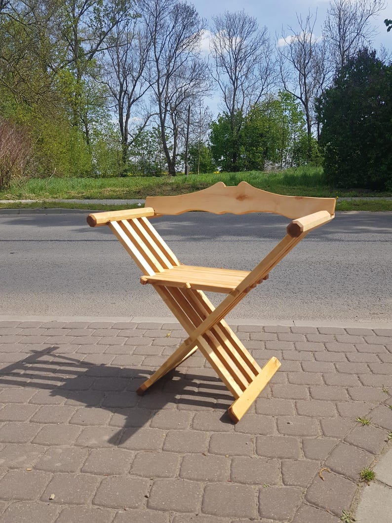 May include: A wooden folding chair with a slatted back and seat. The chair is made of natural wood and has a simple, rustic design.