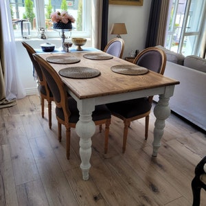 Könnte beinhalten: Ein weißer und hölzerner Esstisch mit vier Stühlen. Der Tisch hat ein weiß lackiertes Gestell und eine Holzplatte. Die Stühle sind mit einem dunkelgrauen Stoff bezogen. Der Tisch ist mit vier Platzsets und einem Mittelstück gedeckt.