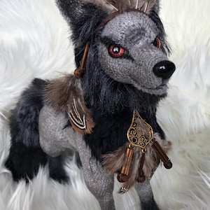 May include: A gray and black plush wolf with a feathered headdress and a beaded necklace. The wolf has red eyes and a fierce expression.