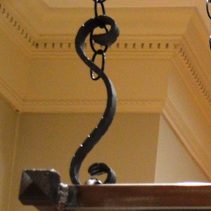 May include: A black metal chain with a decorative hook at the end. The hook is shaped like a stylized 'S' and is attached to a wooden surface.