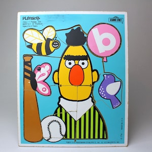 Può includere: Un puzzle di legno a tema Sesame Street con Bert dello show. Il puzzle ha 11 pezzi ed è consigliato per bambini dai 2 ai 5 anni. Il puzzle include una mazza da baseball, una palla da baseball, una farfalla, un uccello, un'ape e un palloncino con la lettera "b" sopra.