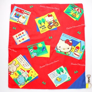 Könnte beinhalten: Rote Stofftasche mit einem bunten Aufdruck mit Hello Kitty und anderen Sanrio-Charakteren. Die Tasche hat einen blauen und gelben Saum und einen gelben Reißverschluss mit einem silbernen Schlüsselanhänger.