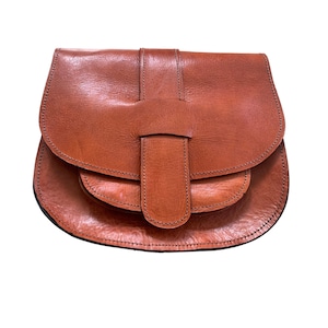 May include: A brown leather saddlebag with a flap closure and a buckle. The bag has a rounded shape and a textured surface. The stitching is visible along the edges of the bag.