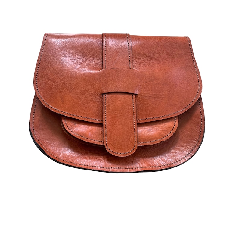 May include: A brown leather saddlebag with a flap closure and a buckle. The bag has a rounded shape and a textured surface. The stitching is visible along the edges of the bag.