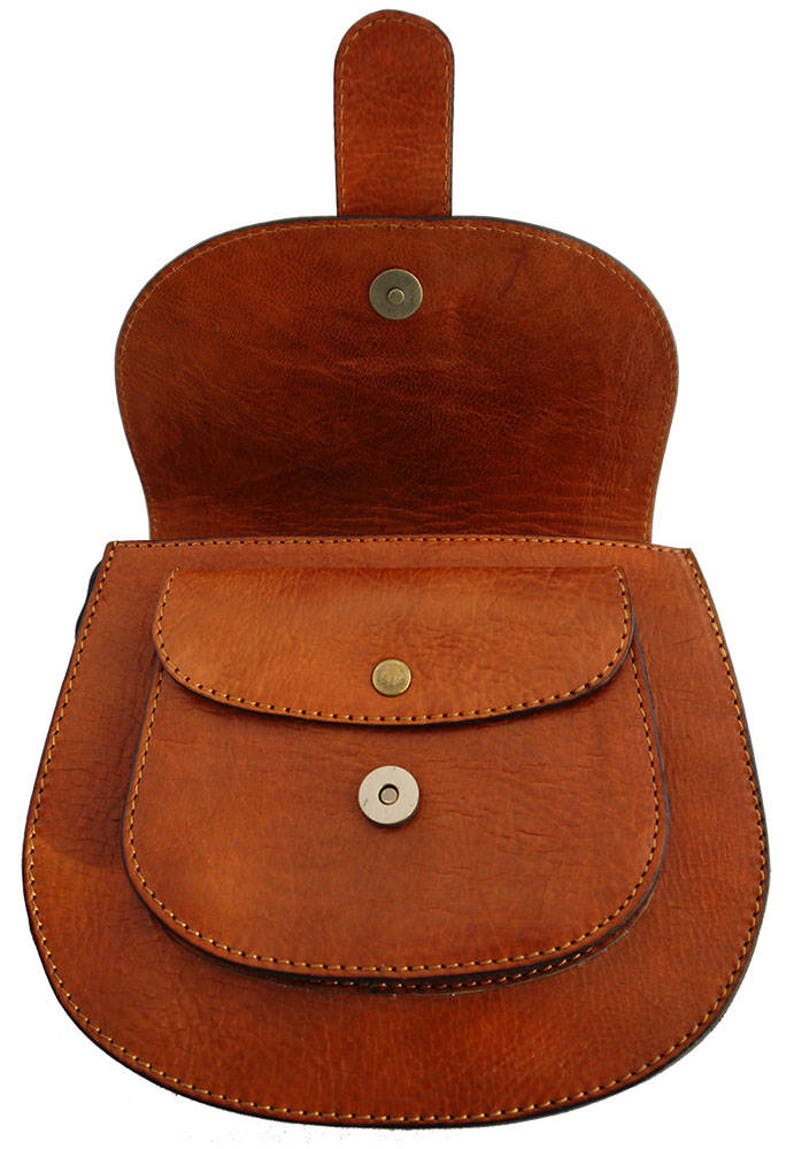 May include: A brown leather saddlebag with a flap closure and a small front pocket. The bag has a rounded shape and a handle on top. The bag is made of a smooth, textured leather and has a magnetic snap closure.