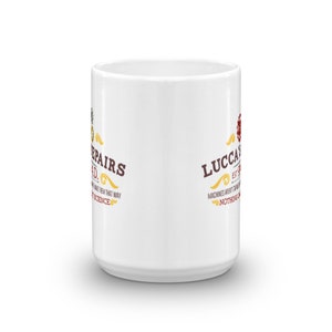 May include: White ceramic mug with the text "Lucca's Repairs" in brown and gold lettering. The mug has a cylindrical shape and a handle. The text includes the phrase "Machines aren't magic, nothing is".