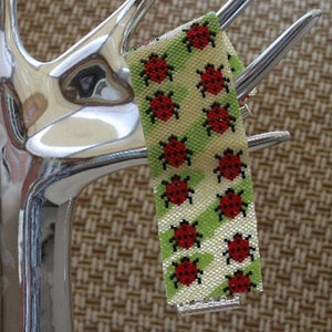 Peut inclure: Un bracelet en perles avec un motif de coccinelles rouges sur fond vert et blanc.