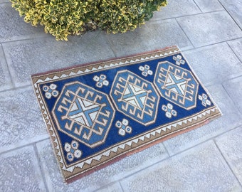 May include: A rectangular, hand-woven rug with a geometric pattern. The rug features a deep blue central field with light blue and cream-colored geometric shapes. The border is a mix of brown and cream, creating a contrasting frame. The rug's dimensions are approximately 24 x 36 inches.