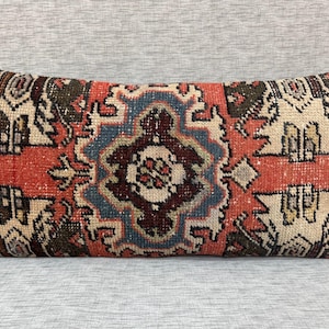 May include: A rectangular pillow with a red, blue, and white patterned design. The pillow is made of a woven fabric with a distressed look.