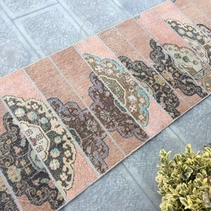 May include: A pink and brown vintage runner rug with a geometric pattern. The rug is made of woven fabric and has a distressed look.