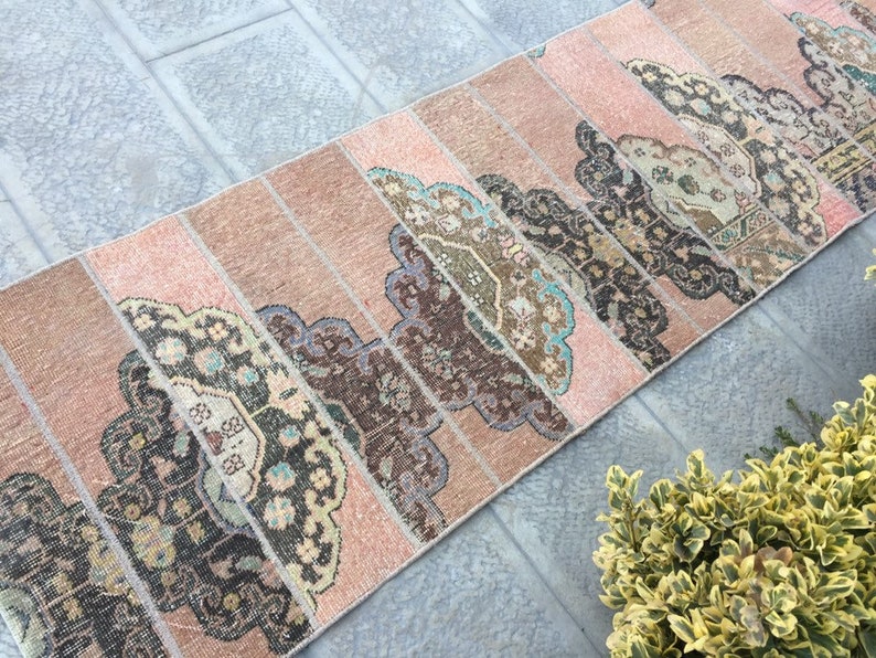 May include: A pink and brown vintage runner rug with a geometric pattern. The rug is made of woven fabric and has a distressed look.