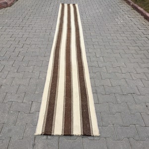 Puede incluir: Una alfombra larga y estrecha de rayas blancas y marrones. La alfombra est&aacute; hecha de un material tejido y tiene un borde con flecos.