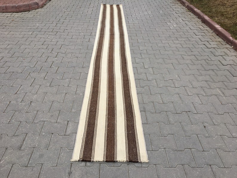 Puede incluir: Una alfombra larga y estrecha de rayas blancas y marrones. La alfombra est&aacute; hecha de un material tejido y tiene un borde con flecos.