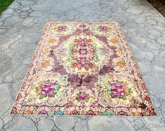 Puede incluir: Una alfombra rectangular con un diseño floral y un medallón central. La alfombra presenta un fondo burdeos oscuro con un centro y bordes color crema. El patrón floral incluye flores moradas, rojas y naranjas, con hojas verdes.