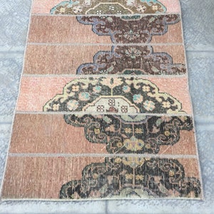 May include: A vintage rug with a pink and brown color scheme. The rug has a geometric pattern with intricate details. The rug is made of wool and has a soft texture.