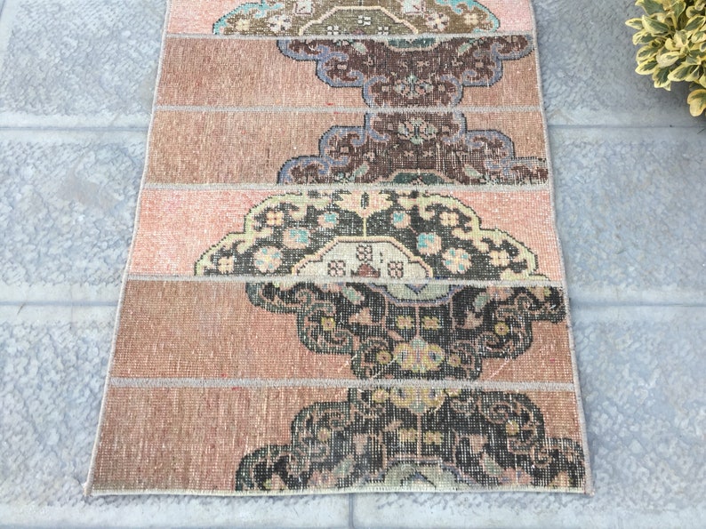 May include: A vintage rug with a pink and brown color scheme. The rug has a geometric pattern with intricate details. The rug is made of wool and has a soft texture.