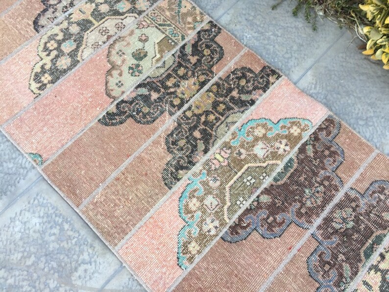 May include: A vintage pink and brown rug with a geometric pattern. The rug has a faded look and is made of woven fabric.