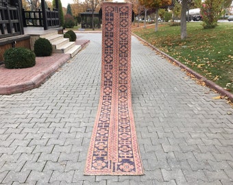 May include: A long, narrow rug with a geometric pattern in shades of pink, orange, and black. The rug is folded in half and lying on a gray brick walkway.