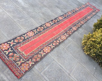 May include: A long, narrow red and black rug with a floral pattern. The rug has a central red stripe and is fringed on both ends.