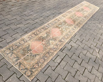 May include: A long, rectangular rug with a faded, vintage look. The rug has a cream background with a repeating pattern of pink, green, and black floral motifs.