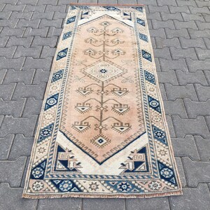 Puede incluir: Una alfombra de pasillo vintage con fondo beige y un patrón geométrico azul y blanco. La alfombra tiene un borde con flecos.