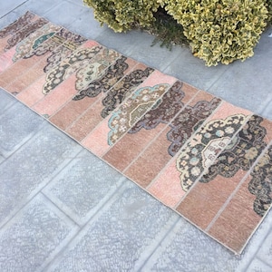 Puede incluir: Una alfombra de pasillo larga y estrecha con un diseño de patchwork. La alfombra está hecha de diferentes piezas de tela en tonos de rosa, marrón y beige. La alfombra tiene un aspecto y una sensación vintage.
