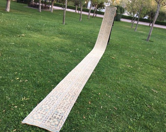May include: A long, cream-colored rug with a geometric pattern in shades of blue, brown, and beige. The rug is laid out on a green grassy lawn.