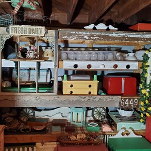May include: A miniature wooden shop with a sign that reads "Fresh Daily". The shop has shelves with various items, including a red miniature refrigerator, a yellow miniature chest of drawers, and a white miniature basket. The shop is decorated with green and yellow floral accents.