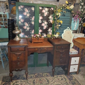 May include: A vintage wooden vanity with two side cabinets, each with drawers and ornate detailing. The vanity is brown, with a floral patterned backdrop and decorative elements, suggesting a classic, antique style.