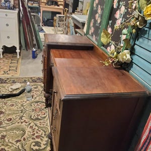 May include: A dark brown antique desk with drawers and a top surface. The desk has a classic design with ornate hardware and a rich wood grain. The desk is in a room with other antique furniture and decor.