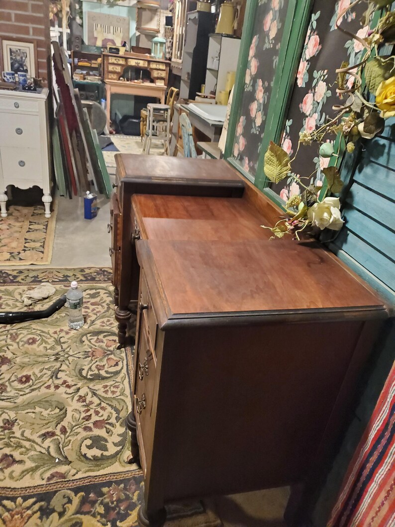 May include: A dark brown antique desk with drawers and a top surface. The desk has a classic design with ornate hardware and a rich wood grain. The desk is in a room with other antique furniture and decor.