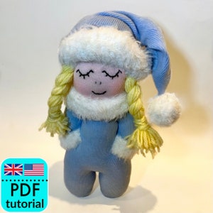 Op de afbeelding: Een blauwe sokpop met een witte bontmuts en een blauwe gebreide muts met een witte pompon. De pop heeft geel garenhaar en een glimlachend gezicht.