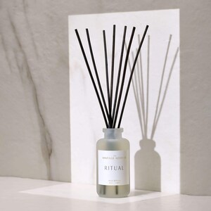 May include: A frosted glass diffuser bottle with black reeds and a white label that reads "The Vintage Advisor" and "Ritual" in gold lettering. The bottle is sitting on a white surface.