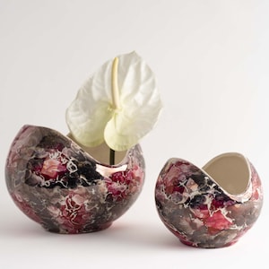 May include: Two ceramic vases with a marbled design in shades of pink, black, and white. The larger vase has a white flower inside.