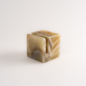 Könnte beinhalten: Ein beige-brauner Marmor-Stiftständer mit einem Schlitz zum Halten eines Telefons oder Tablets. Der Ständer hat eine geometrische Form und eine natürliche Steinoberfläche.