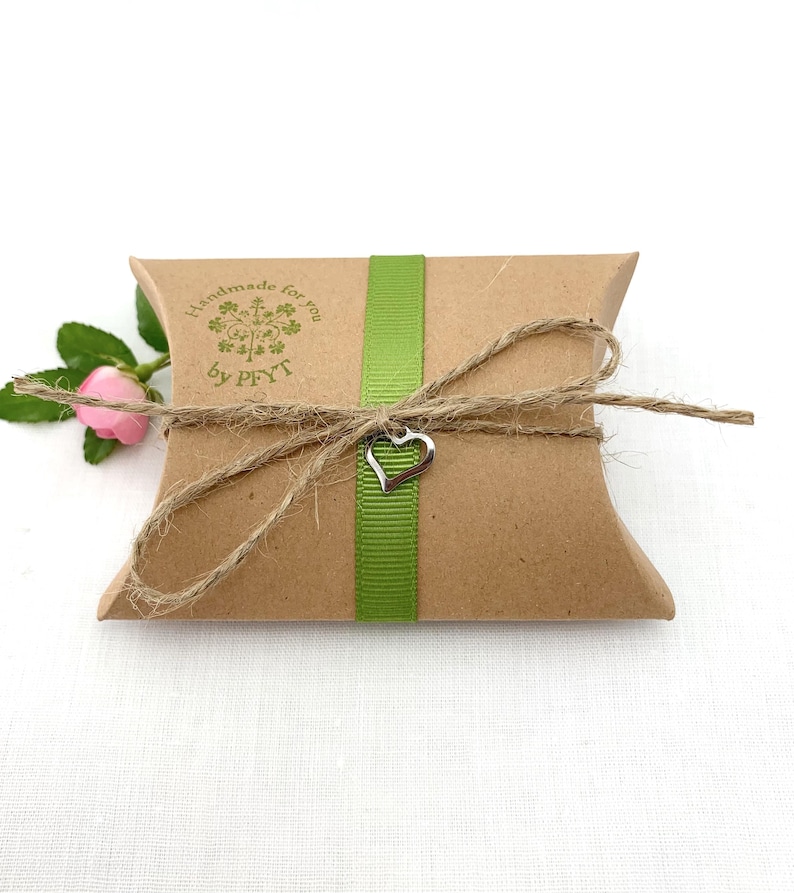 K&ouml;nnte beinhalten: Eine braune Geschenkbox aus Papier mit einem gr&uuml;nen Band und einem silbernen Herzanh&auml;nger. Die Box ist mit Schnur gebunden und hat einen Stempel mit der Aufschrift "Handmade for you by PFYT".
