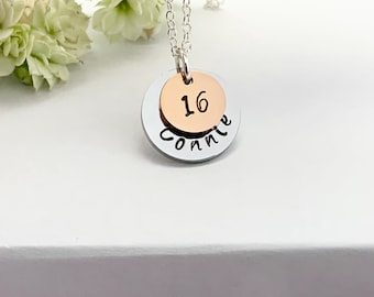 May include: Silver necklace with a double-layered pendant. The top layer is a gold-toned disc with the number "16" engraved on it. The bottom layer is a silver disc with the name "Connie" engraved on it.