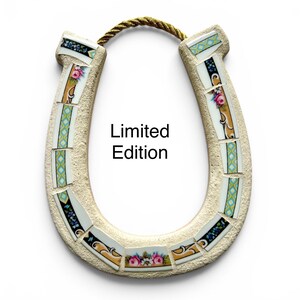 May include: A decorative horseshoe with a mosaic design. The horseshoe is beige with floral and geometric patterned tiles. The text "Limited Edition" is printed on the horseshoe. A gold rope is attached at the top.
