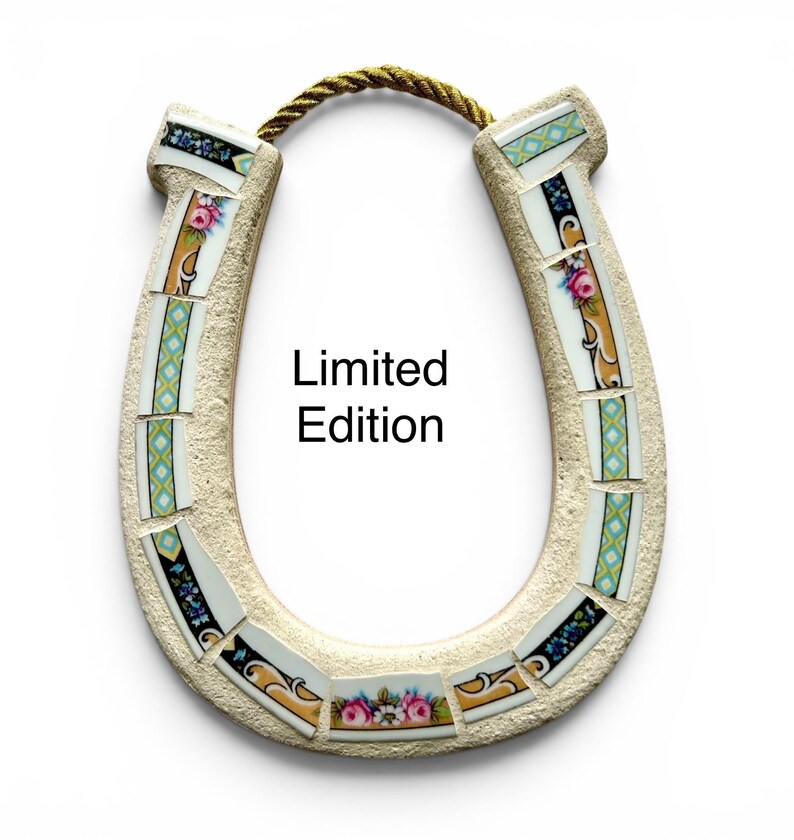 May include: A decorative horseshoe with a mosaic design. The horseshoe is beige with floral and geometric patterned tiles. The text "Limited Edition" is printed on the horseshoe. A gold rope is attached at the top.
