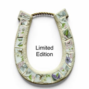May include: A horseshoe-shaped wall hanging made of mosaic tiles. The tiles are decorated with floral patterns in pink, purple, and green. The text "Limited Edition" is printed on the front. A gold rope is attached for hanging.