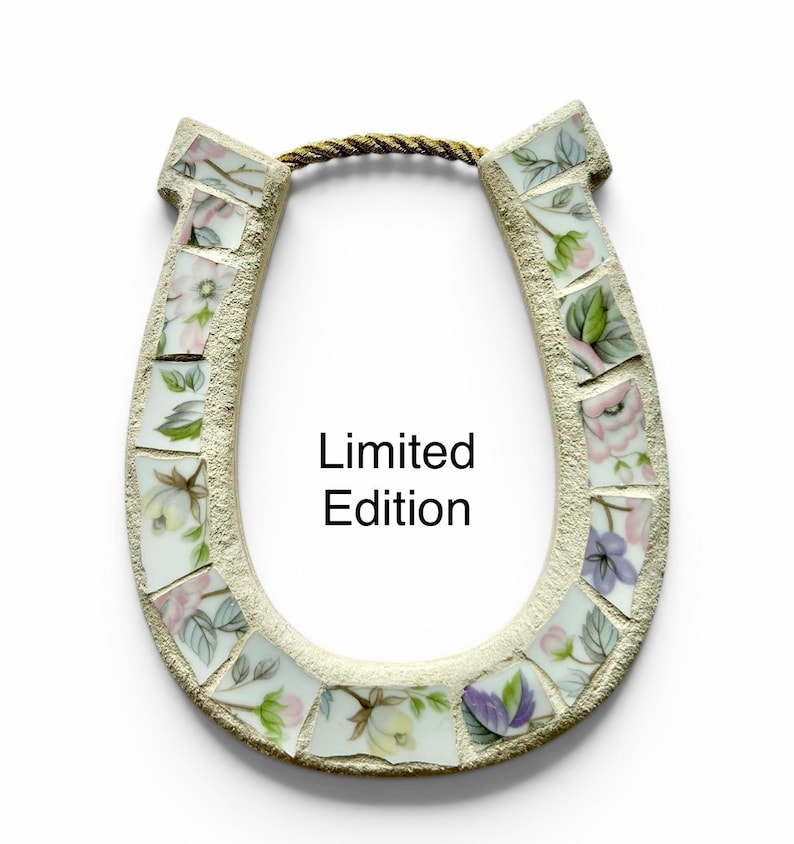 May include: A horseshoe-shaped wall hanging made of mosaic tiles. The tiles are decorated with floral patterns in pink, purple, and green. The text "Limited Edition" is printed on the front. A gold rope is attached for hanging.