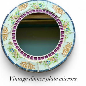 May include: Round mirror with a mosaic border made from vintage dinner plates. The border features floral patterns in blue, pink, and gold, with a purple glitter inner ring and a blue glitter outer edge. The text "Vintage dinner plate mirrors" is at the bottom.